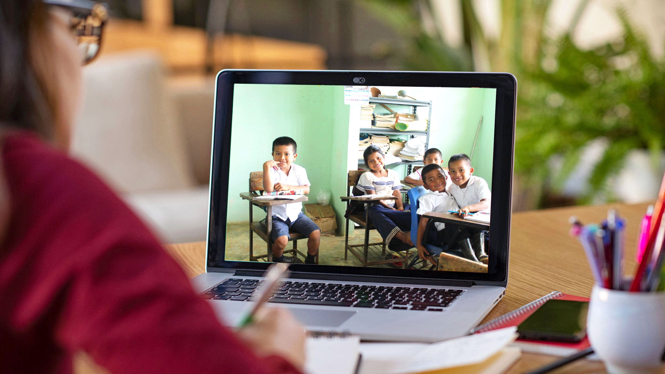 Studying with video online lesson at home Young student watching lesson online and studying from home. Young woman taking notes while looking at computer screen following professor doing math on video call. Latin girl student studying from home and watching teacher explaining math formula on video chat.